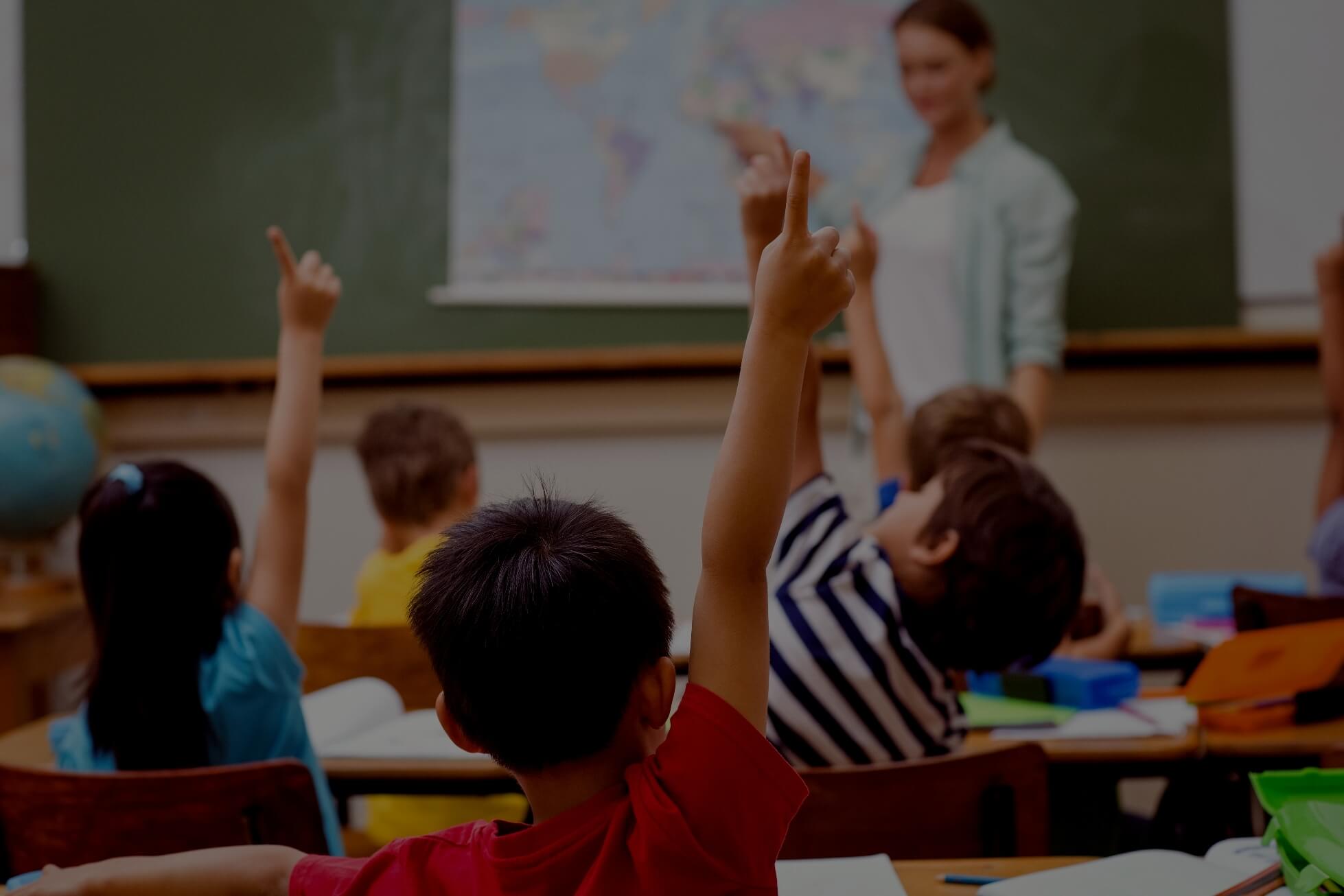 children in classroom raise their hands